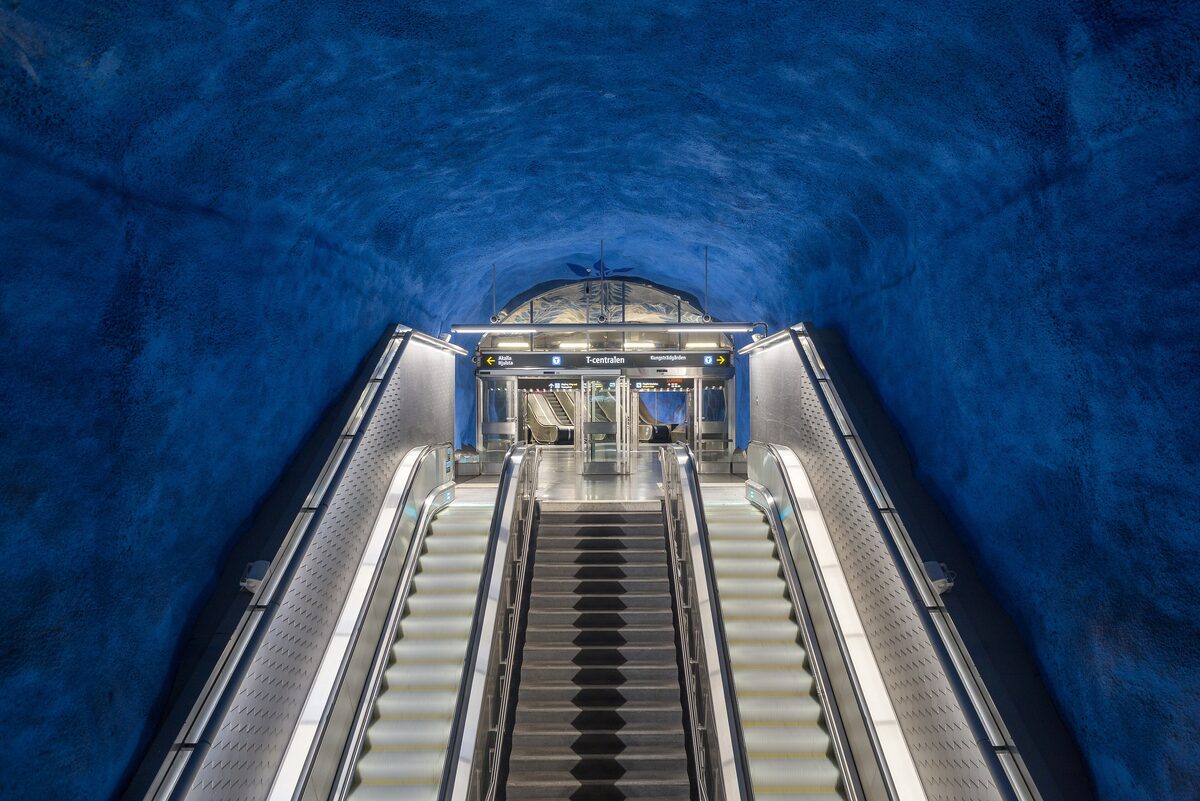 The escalators of T-Centralen metro station under a rough cave ceiling painted blue with leaf patterns