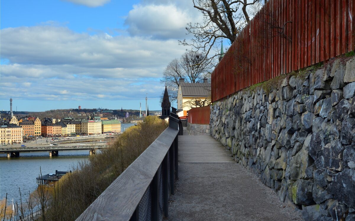 The wooden railing of the Monteliusvägen path on the Södermalm cliffs, with Riddarholmen and Gamla stan across the water