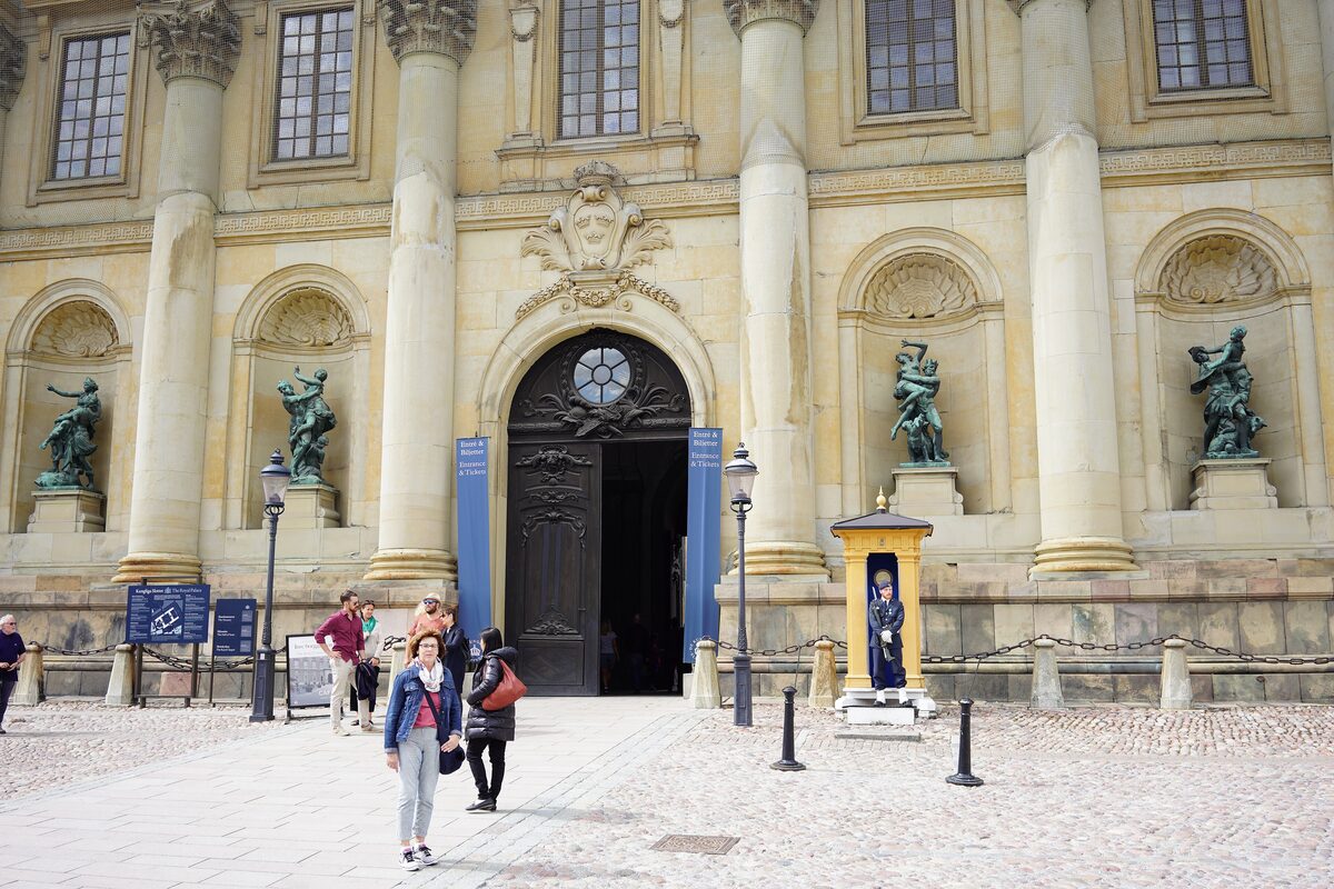 A guard in a sentry box beside the arched entrance of the Royal Palace in Stockholm, with bronze statues in the niches of the facade