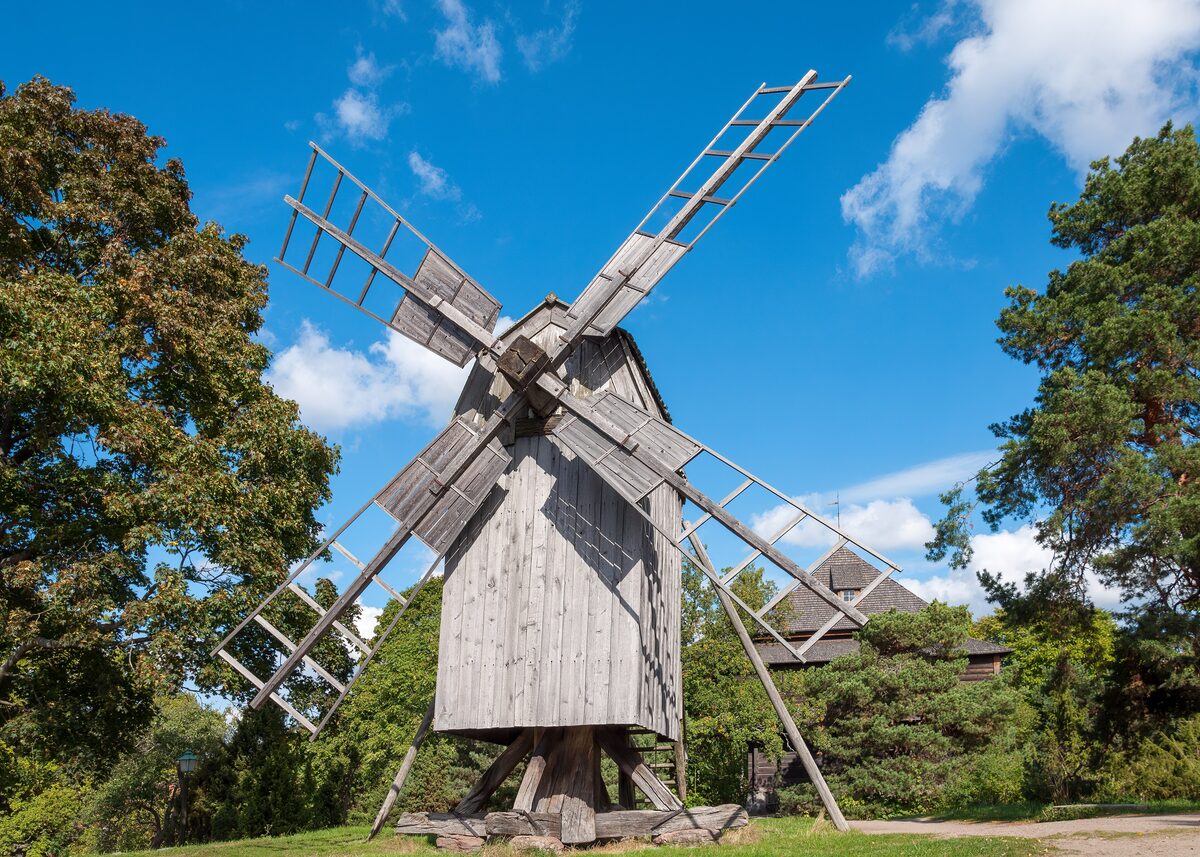 An old wooden windmill on a grassy hill among trees at Skansen open-air museum