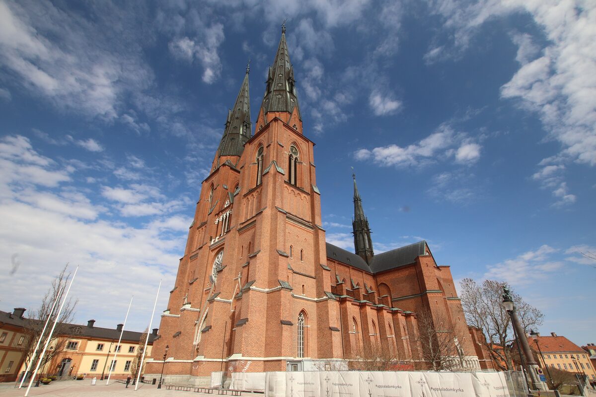 The red-brick Gothic towers of Uppsala Cathedral rising against a blue sky with white clouds