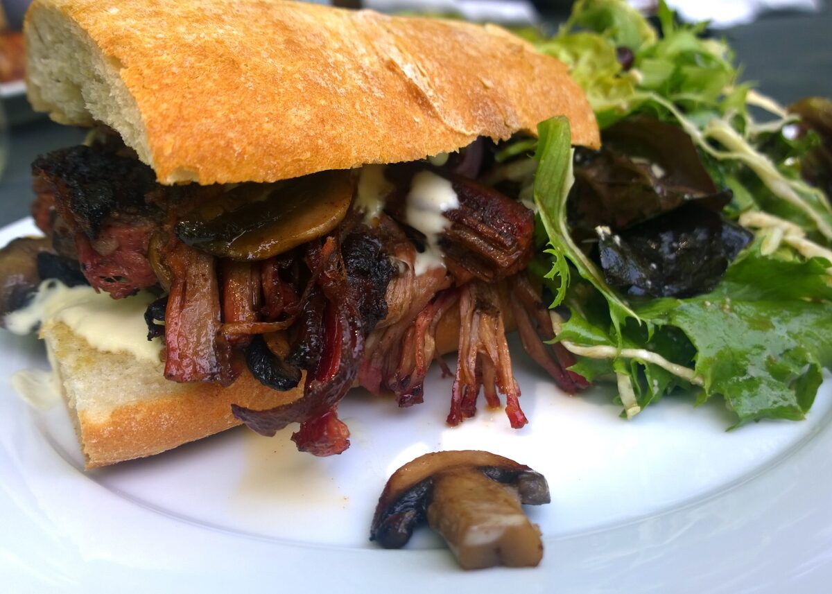 A pulled beef brisket sandwich with mushrooms and salad