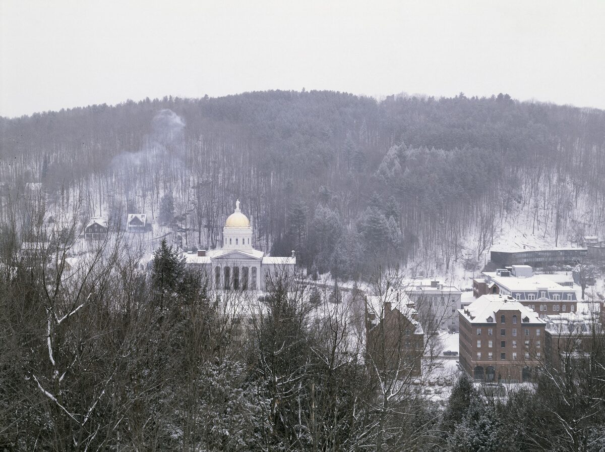 Vermont State House dome above snowy Montpelier rooftops and wooded hills