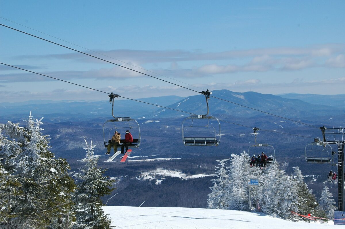 Skiers on chairlifts above frosted trees and distant Vermont hills