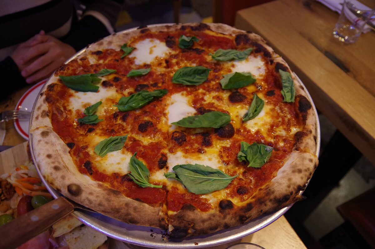 A Margherita pizza with basil on a metal tray