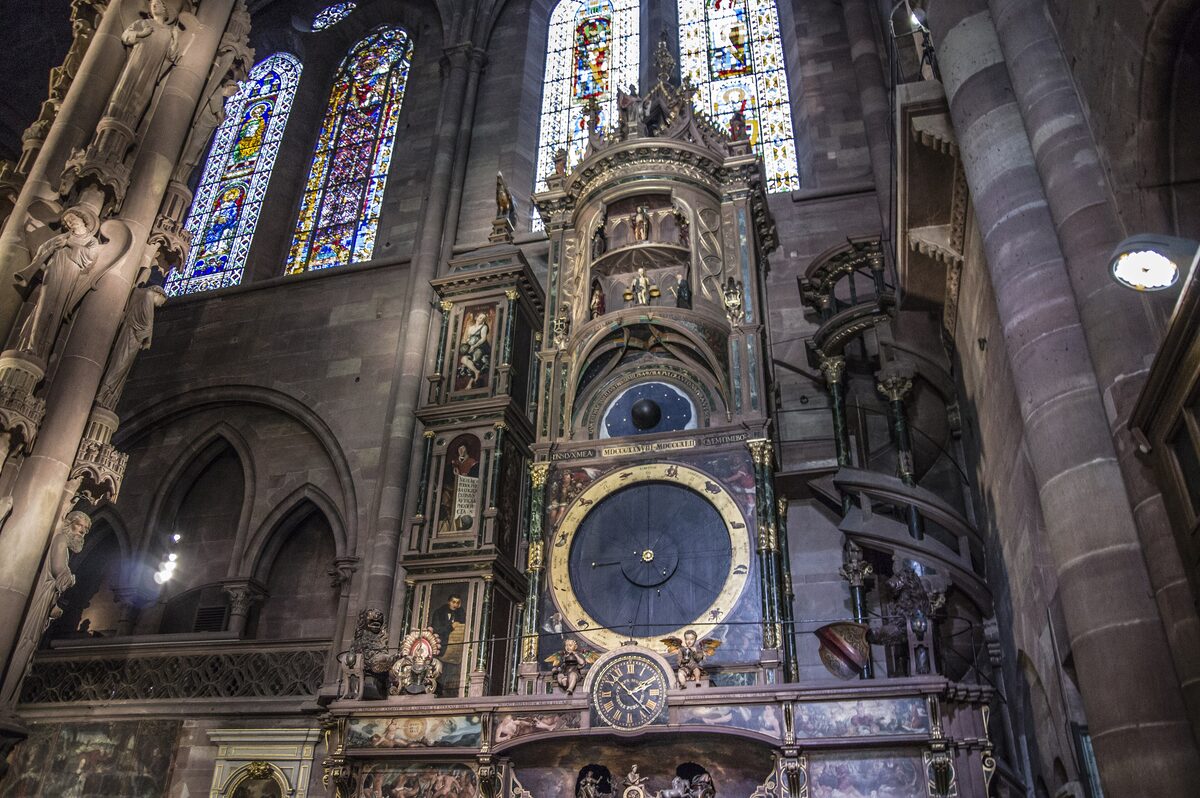 The tall carved case of the astronomical clock inside Strasbourg Cathedral, with its round dial and painted figures set against the stone pillars