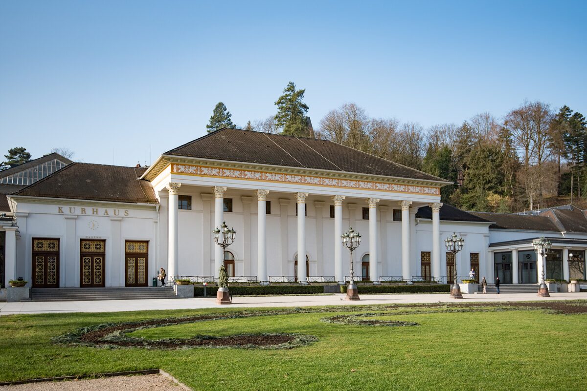 The white columned Kurhaus of Baden-Baden with its gilded frieze, tall windows and lamp posts across a lawn