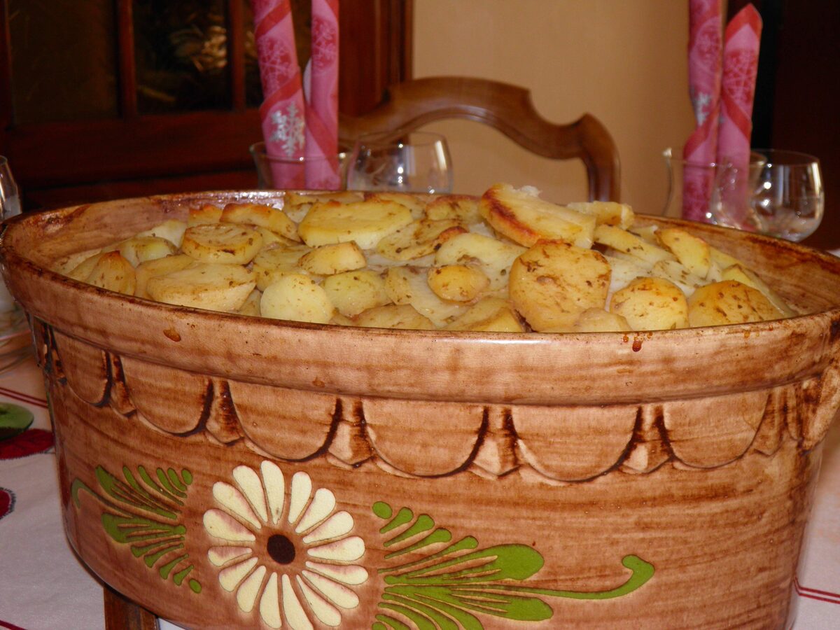 A glazed ceramic dish of baeckeoffe with its sliced potatoes browned on top, on a set table
