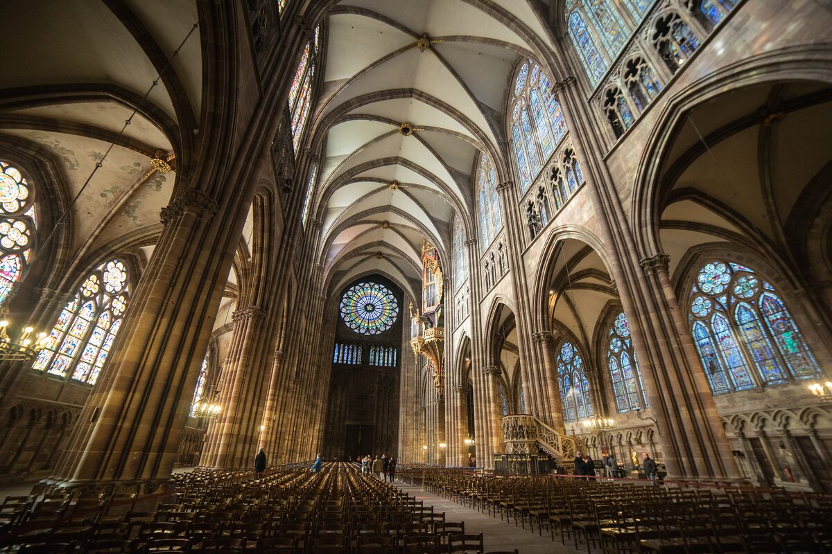 The nave of Strasbourg Cathedral seen from the west end, with rows of chairs, ribbed vaults, stained-glass windows and the west rose window at the far end