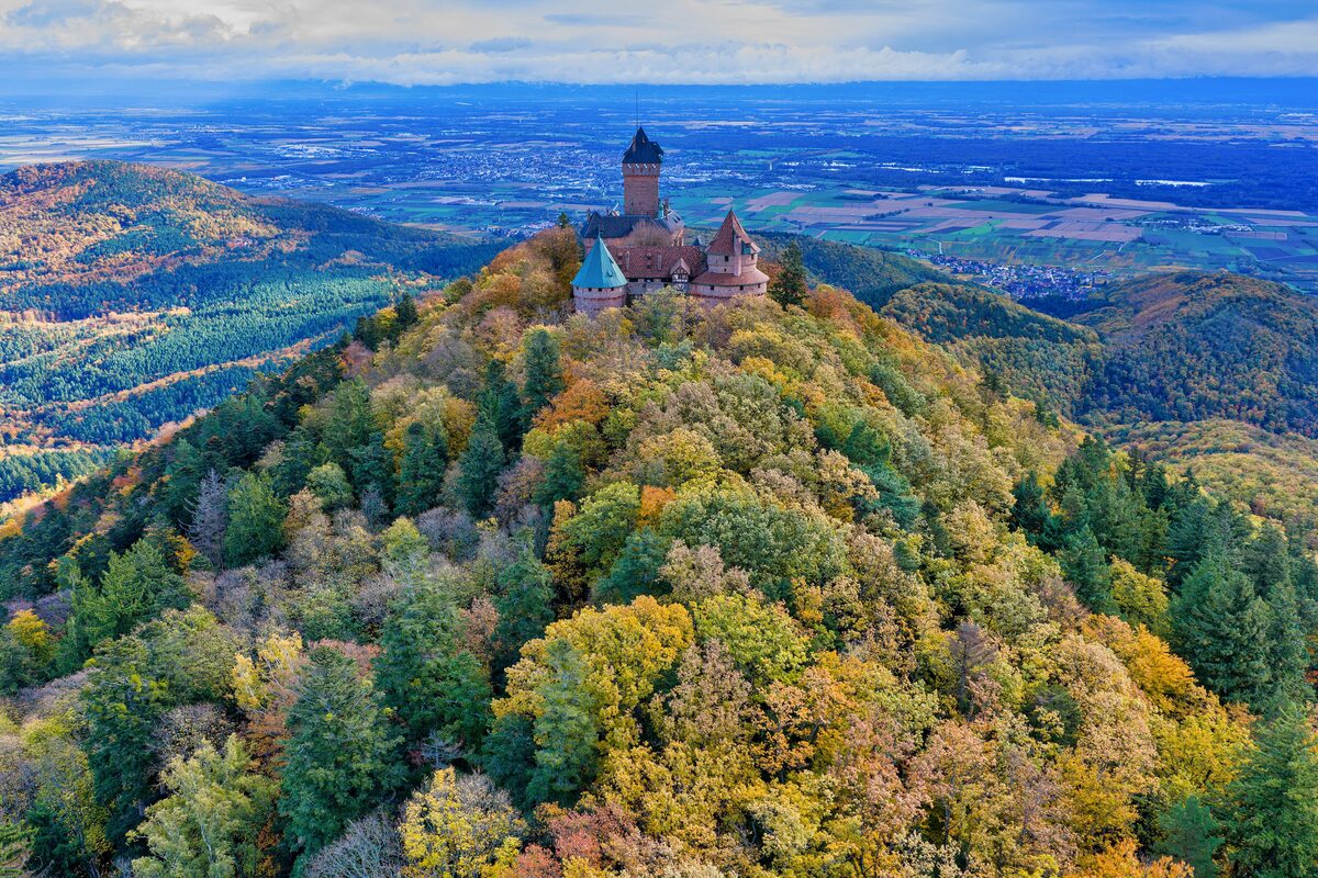 The restored Haut-Kœnigsbourg castle on its wooded hill, seen from the air in autumn with the Rhine plain far behind
