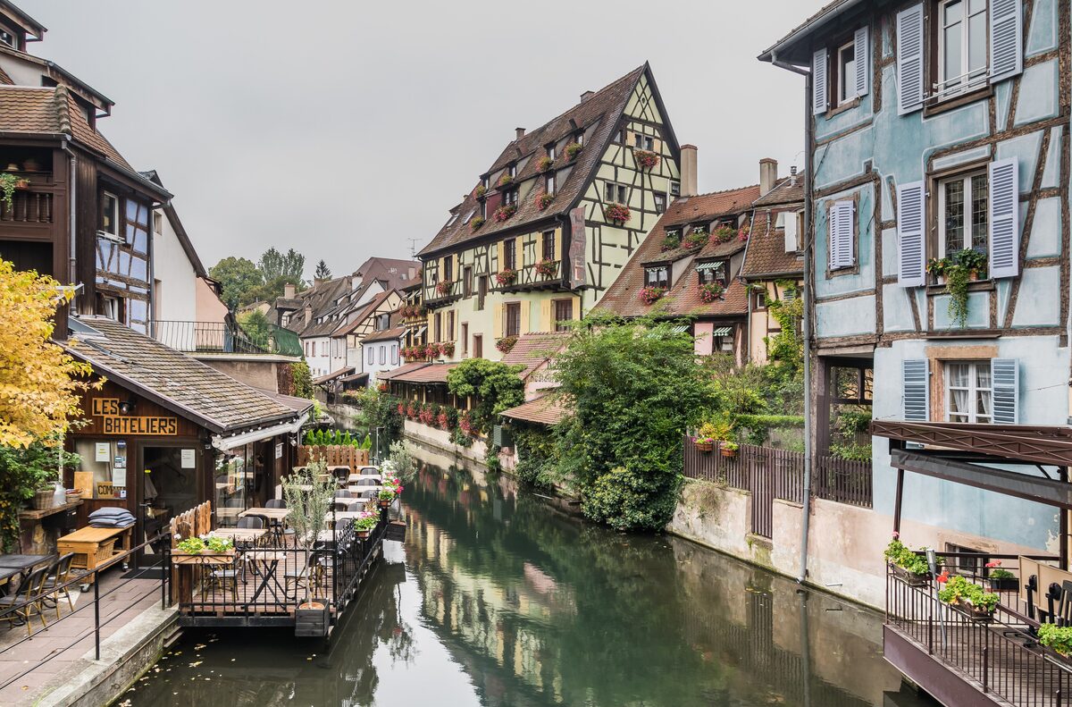 Half-timbered houses and a restaurant terrace on the canal in Little Venice in Colmar, with a railing and tables over the water