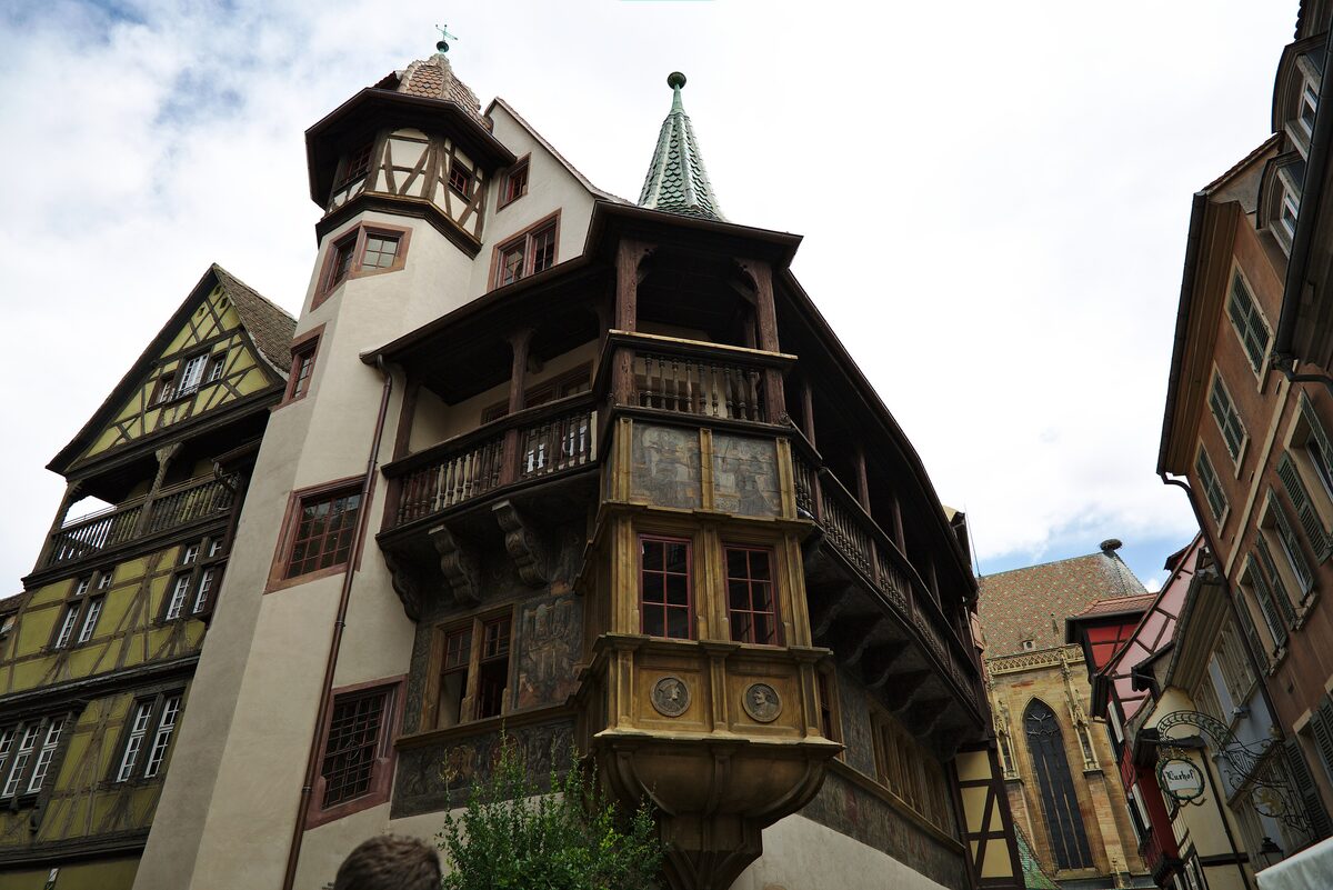The carved oriel and round turret of the Maison Pfister in Colmar, with its painted timber frame against a blue sky