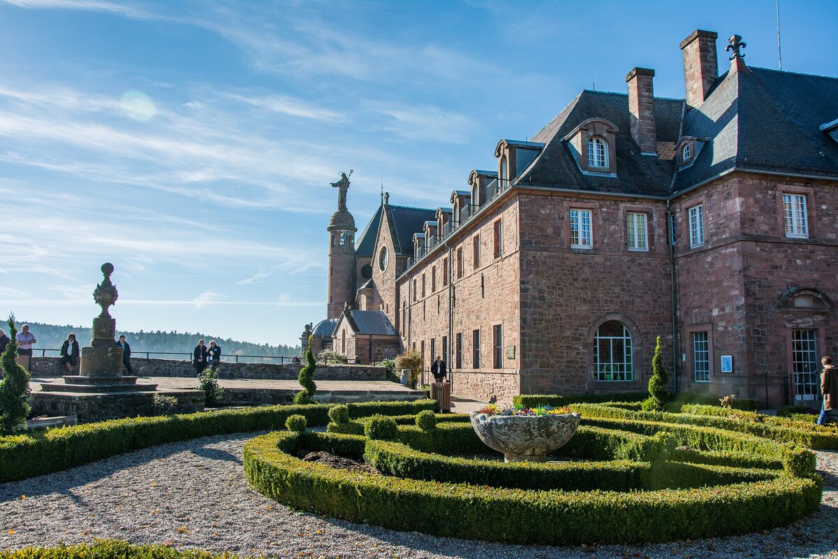 The red sandstone convent of Mont Sainte-Odile behind a clipped box-hedge garden, with the viewing terrace and the statue of Saint Odile beside it