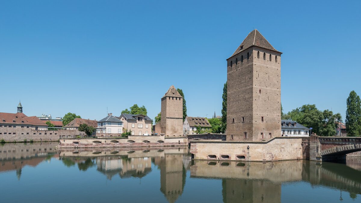 The towers of the Ponts Couverts rising above the river Ill, with their reflections in the still water and a sunny sky
