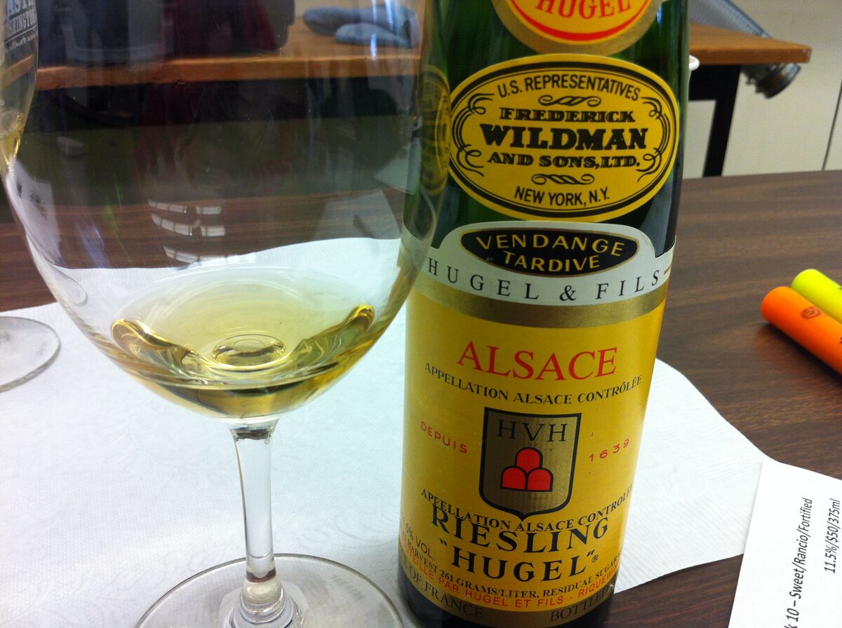 A glass of pale Alsace white wine next to a bottle of Hugel Riesling