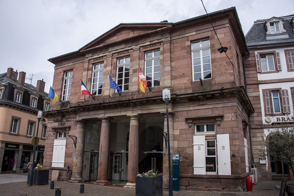 The sandstone Hôtel de Ville of Sélestat on a sunny street, with a row of flags on its front