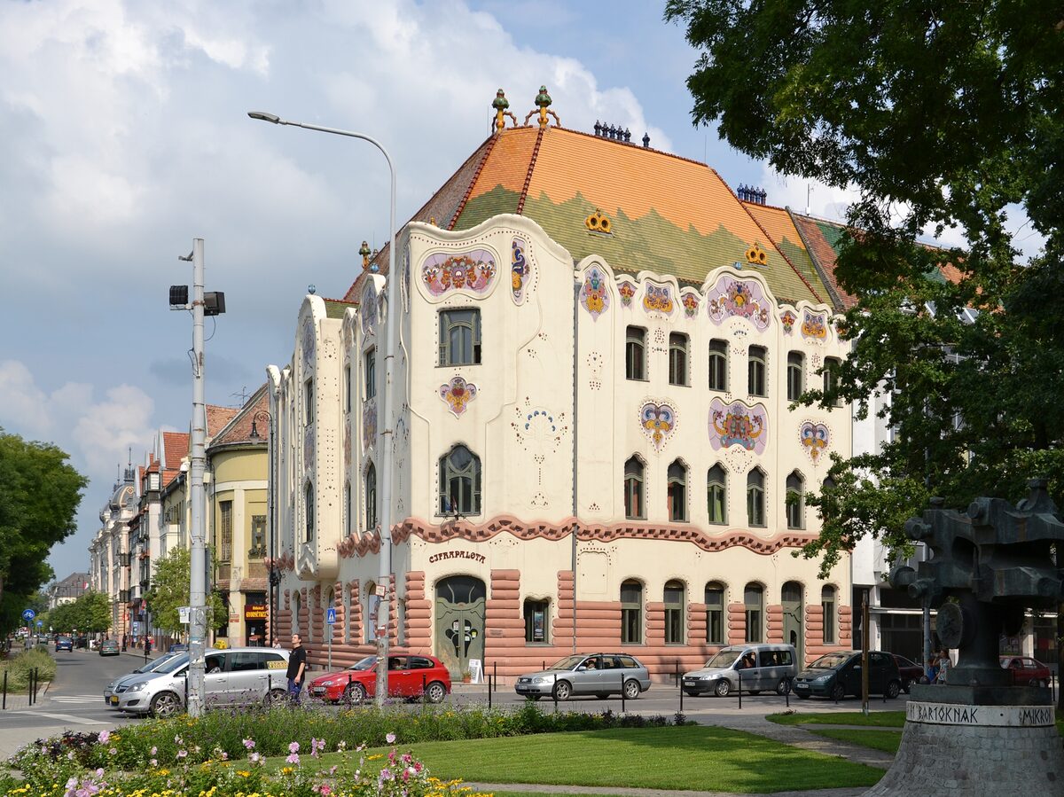 Kecskemét's Cifrapalota, a cream Art Nouveau palace with colorful majolica flowers and a wavy orange-and-green tiled roof