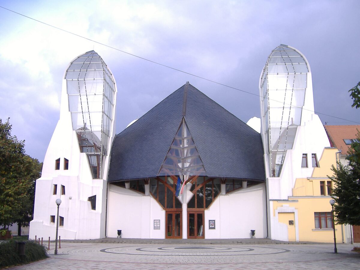 Imre Makovecz's Hagymaház theater in Makó: a steep dark slate roof between two white towers topped with onion-shaped glass spires