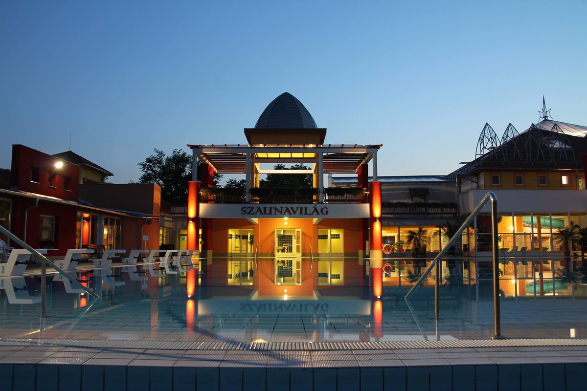 The Szent Erzsébet bath in Mórahalom at dusk, its lit domed pavilion reflected in an outdoor pool