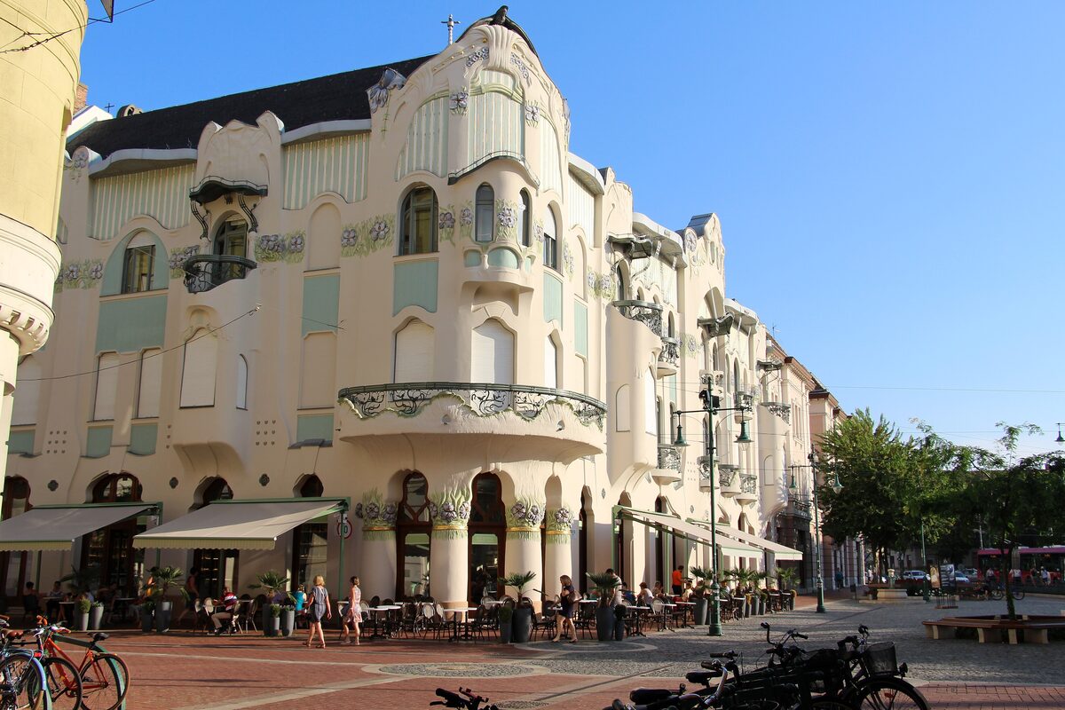 The curving Art Nouveau Reök Palace in pale cream with mint-green details and flower motifs, with café awnings and bicycles in front
