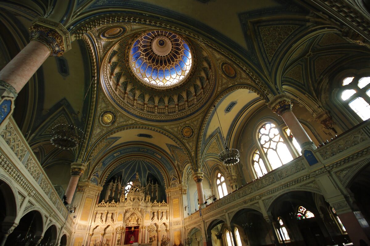 Inside the New Synagogue, looking up at the blue-and-gold glass dome above painted arches, with the gilded Torah ark below