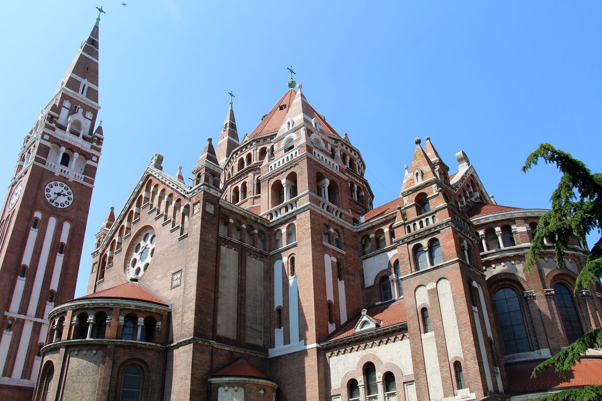 The red-brick Votive Church seen from the side, with its clock tower, domed crossing and rounded apses under a blue sky