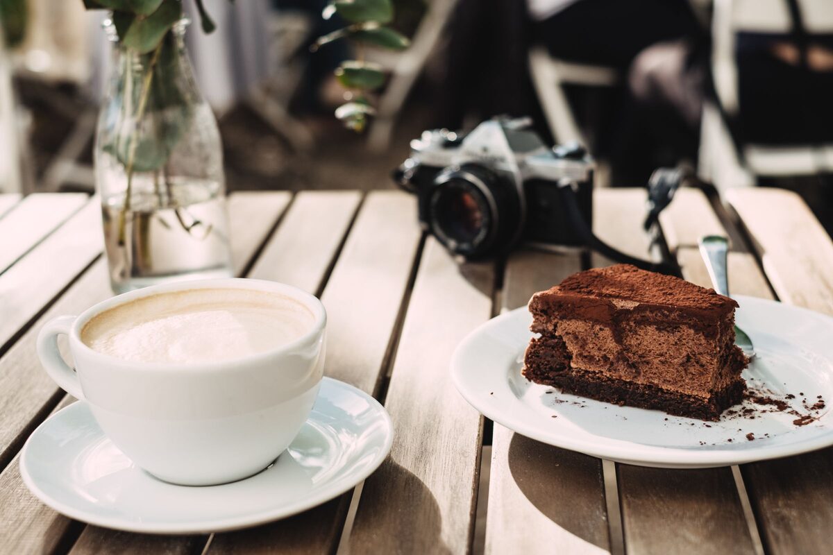 A cup of cappuccino and a slice of chocolate cake on a wooden cafe table
