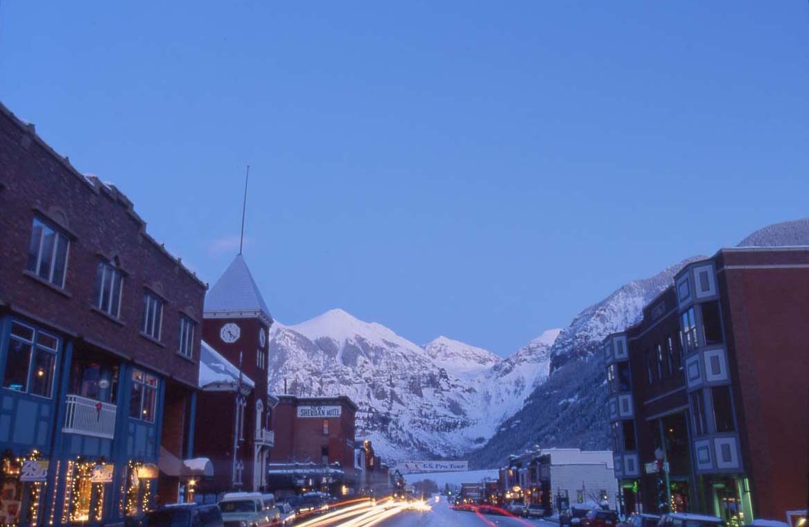 Colorado Avenue at dusk, brick buildings and snowy peaks above Telluride