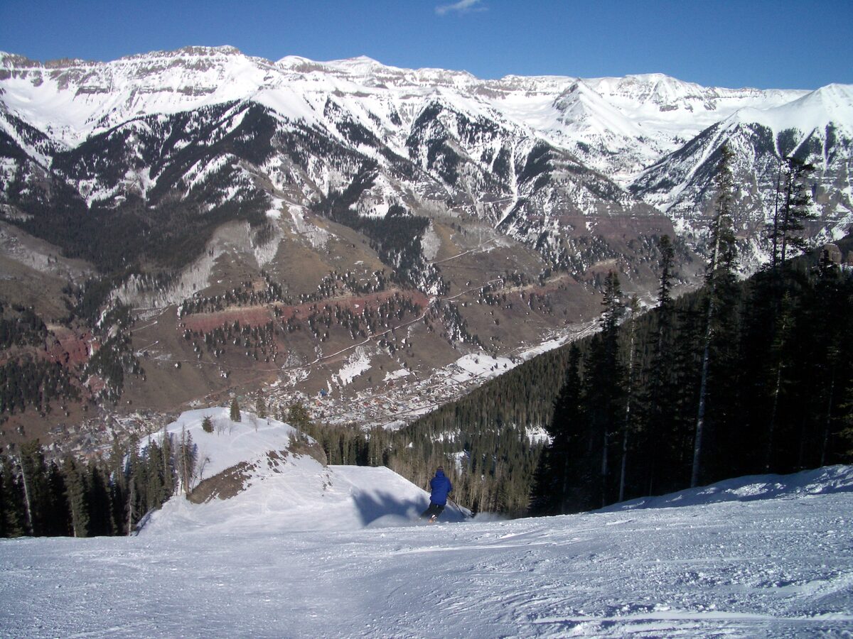 A lone skier on a groomed Telluride run, the town far below