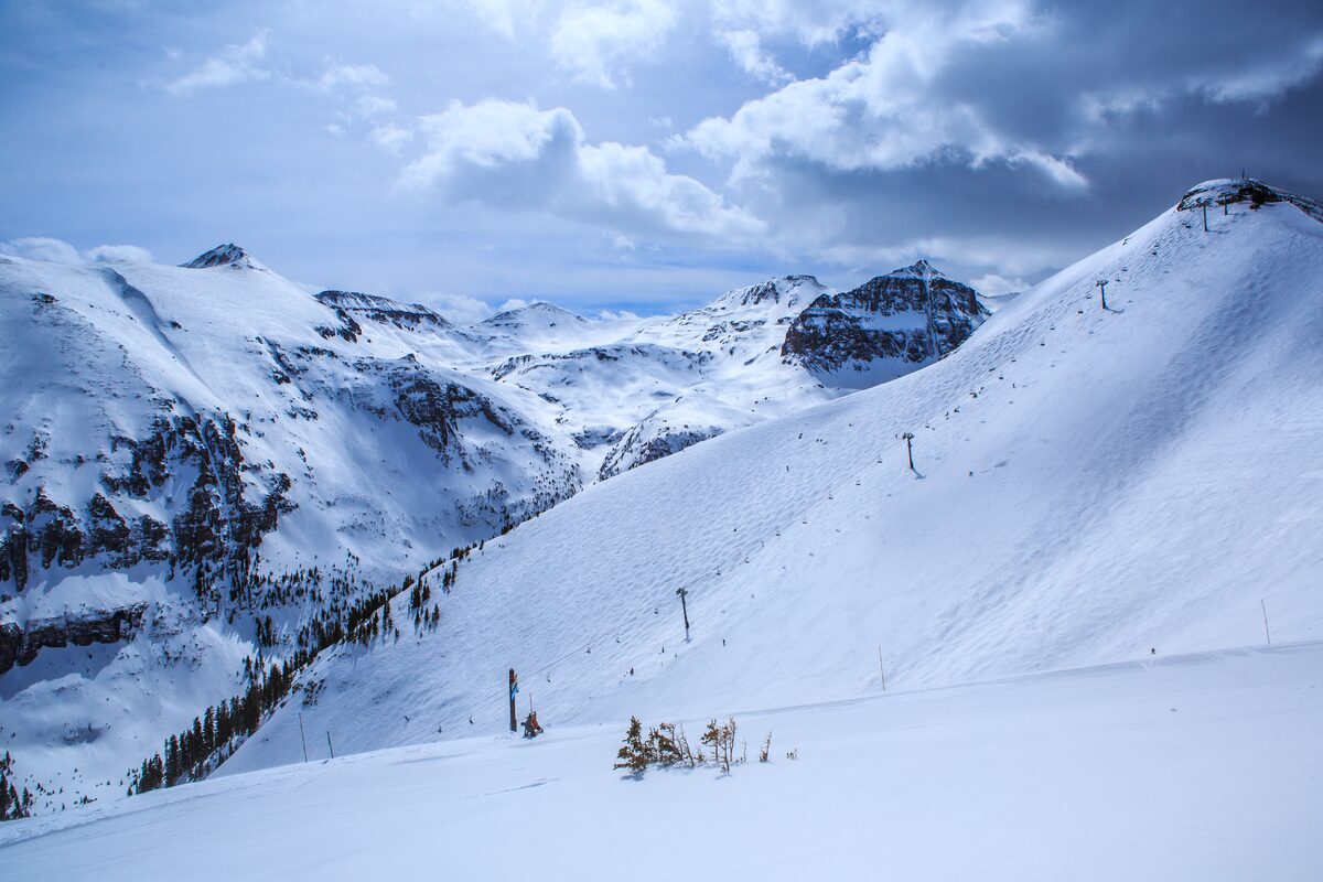A wide snow slope with a lift line below rocky Telluride peaks