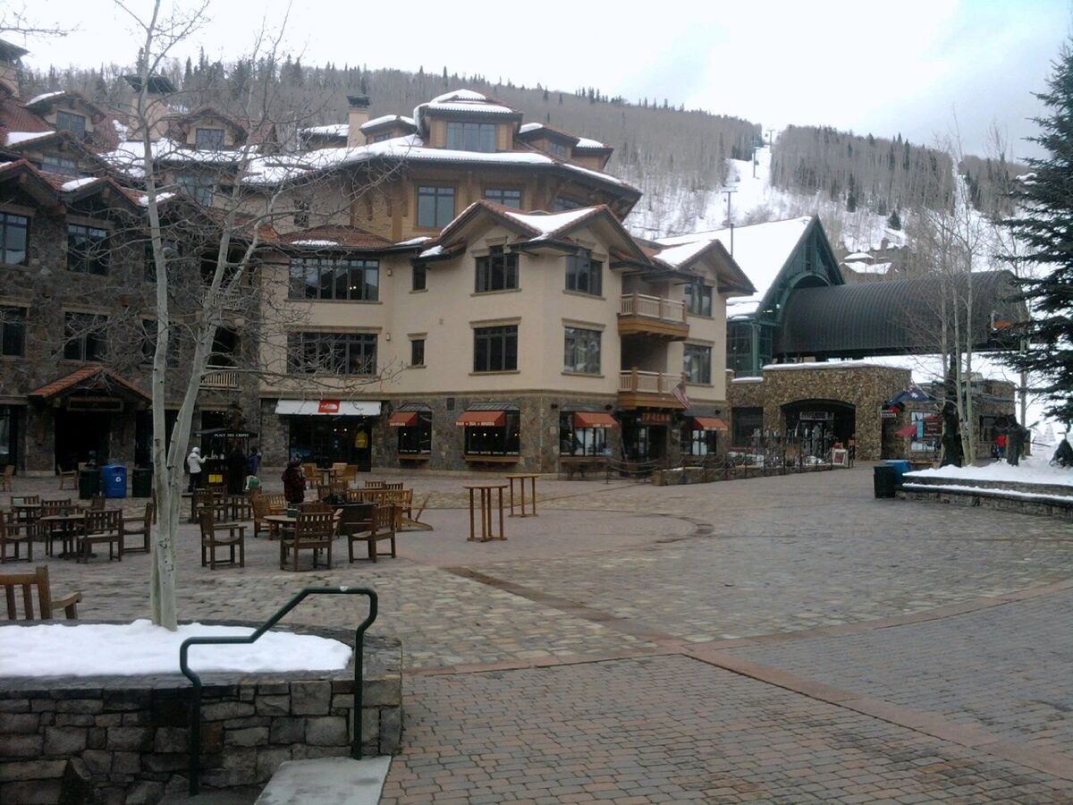 A paved plaza ringed by lodges in Mountain Village, with ski runs behind