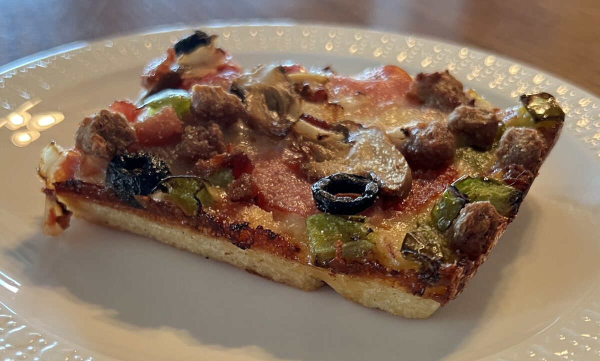 A square slice of Detroit-style pizza with sausage, mushroom and peppers