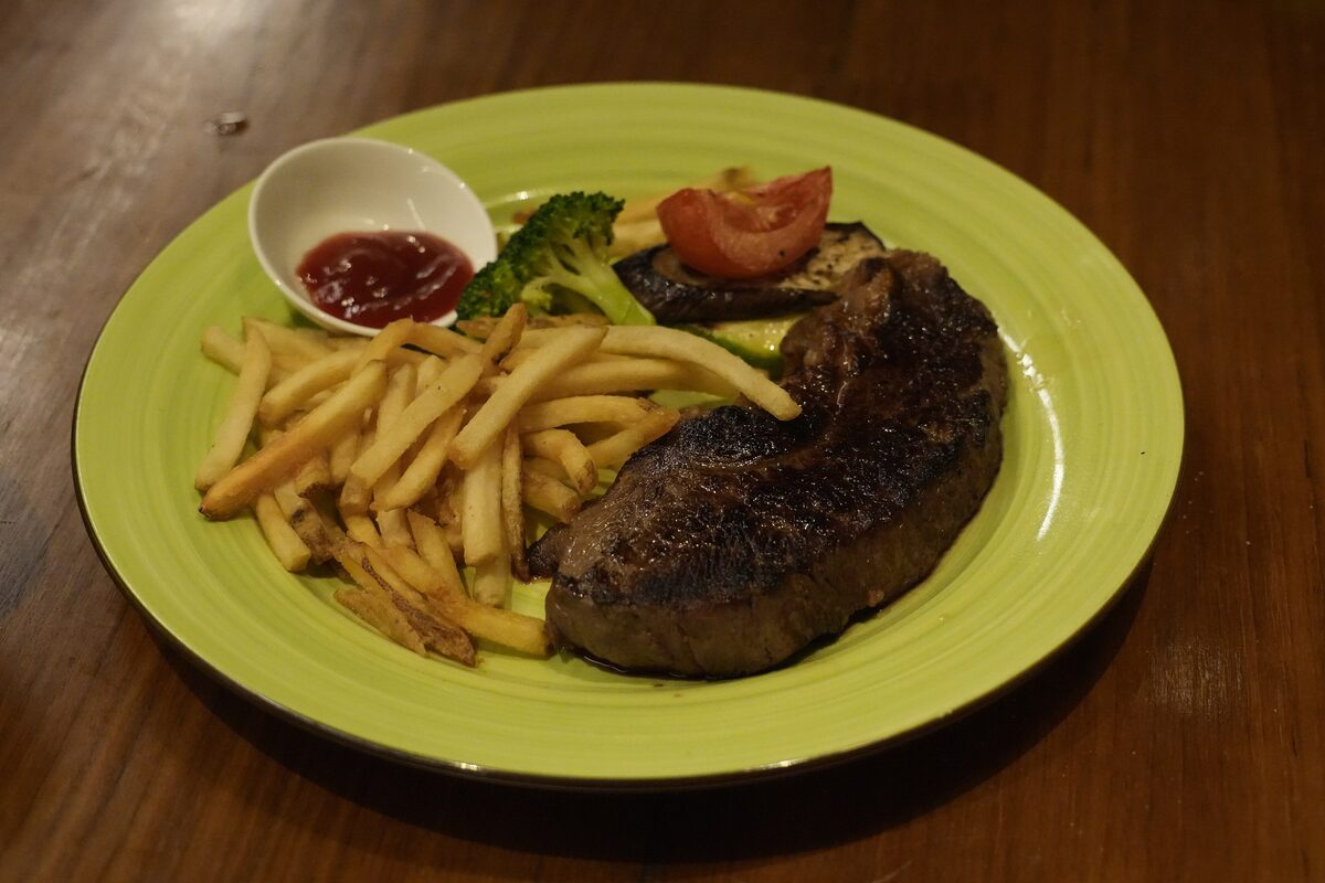 A seared steak with fries and broccoli on a green plate