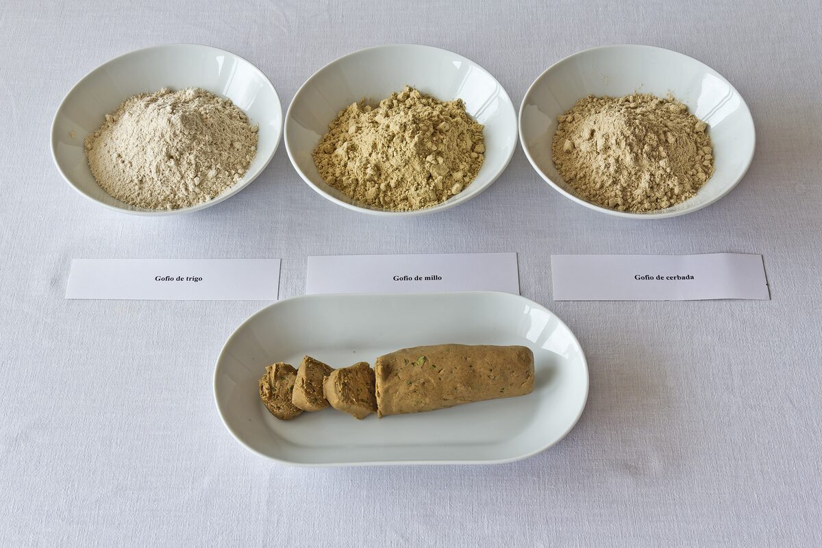 Bowls of gofio flour in three shades and a block of gofio on a plate