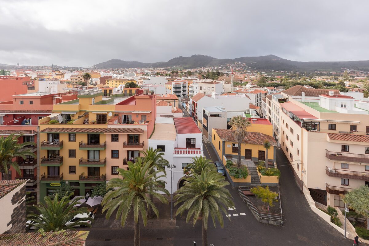 A street of colorful houses in San Cristóbal de La Laguna, with palms and hills behind