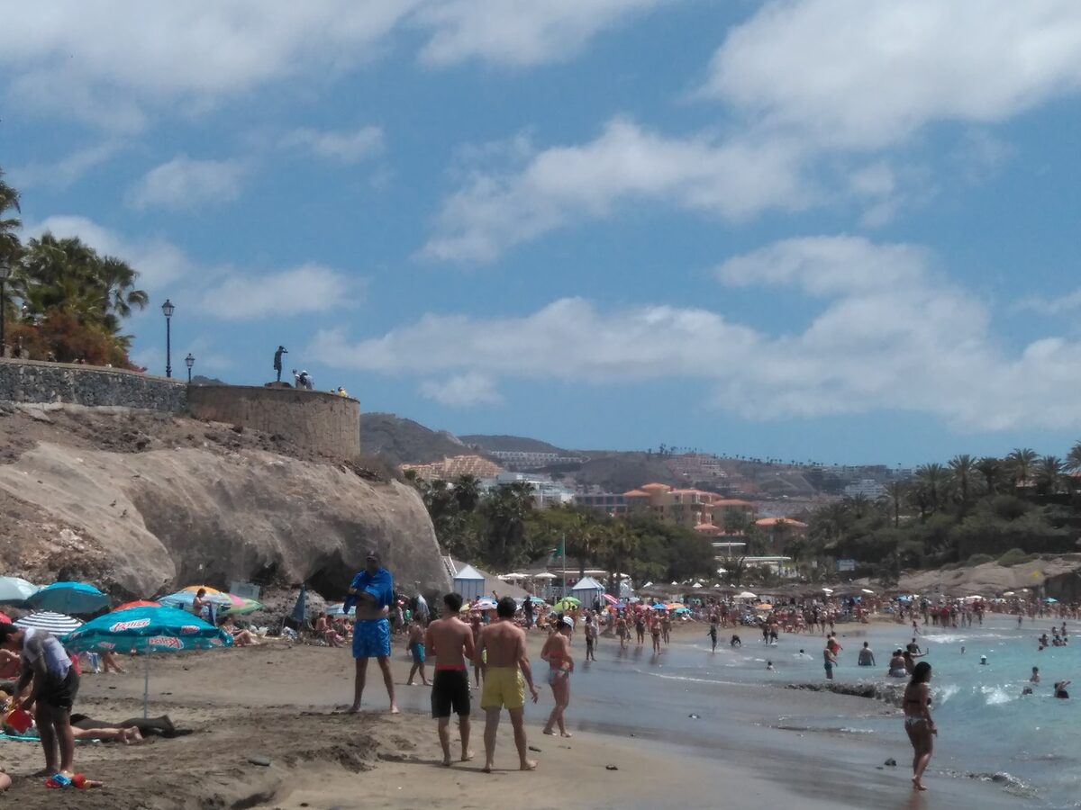 Playa del Duque in Costa Adeje, with pale sand, shallow sea and bathers under a blue sky
