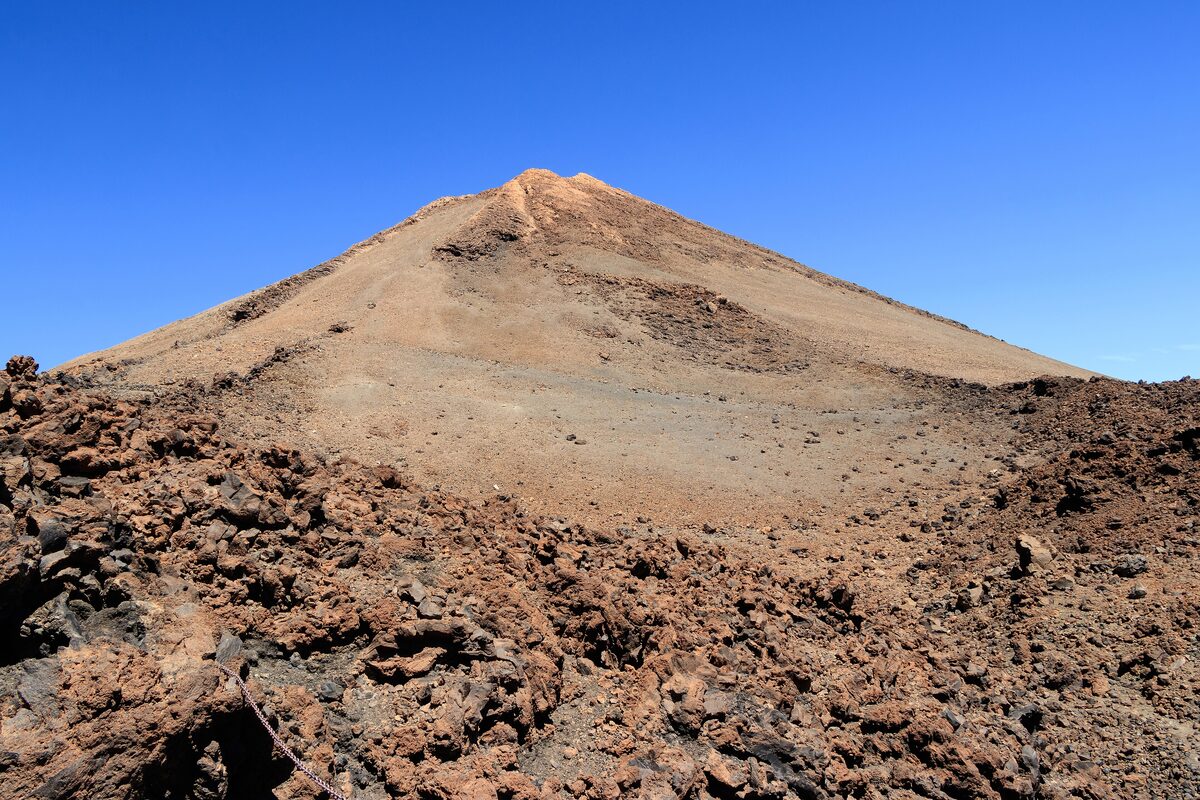 The cone of Pico del Teide under a blue sky, with lava rock in the foreground