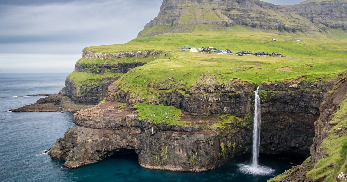 The Múlafossur waterfall dropping off a green cliff into the sea below the village of Gásadalur on Vágar