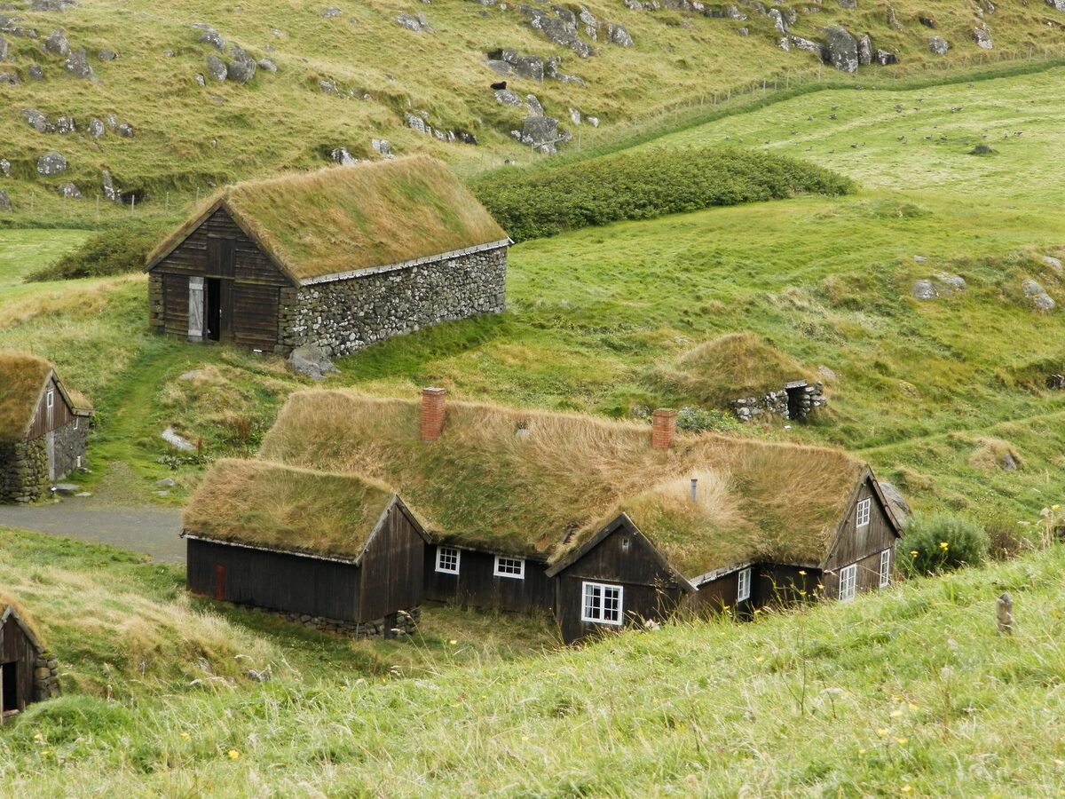 The turf-roofed black wooden farm buildings of Hoyvíksgarður on a green hillside, now an open-air museum