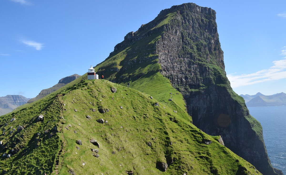 The Kallur lighthouse on a grassy ridge above the sea, with a tall cliff beside it