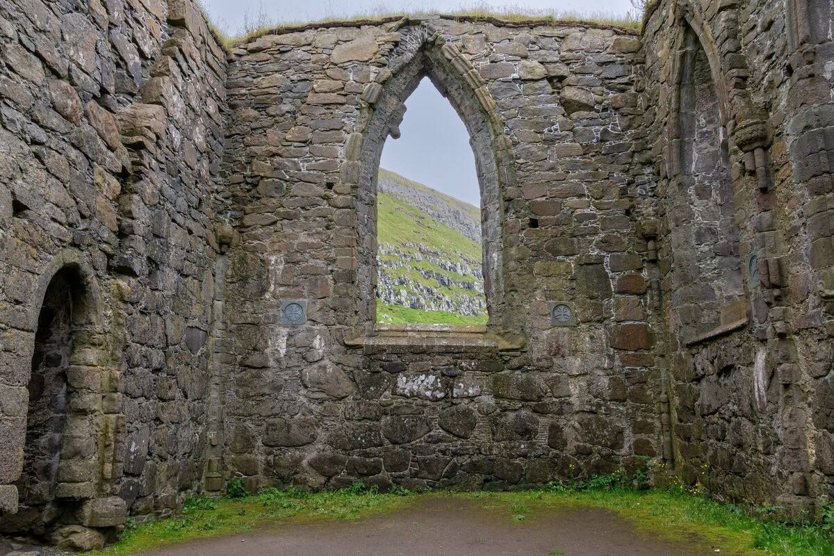 The ruined interior of Magnus Cathedral in Kirkjubøur, framed by a tall Gothic window