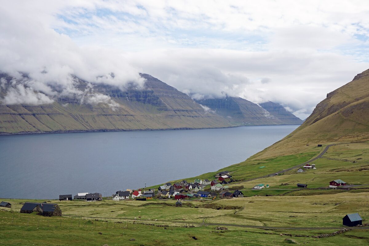 The small village of Mikladalur on Kalsoy by the fjord, with cloud-capped mountains across the water