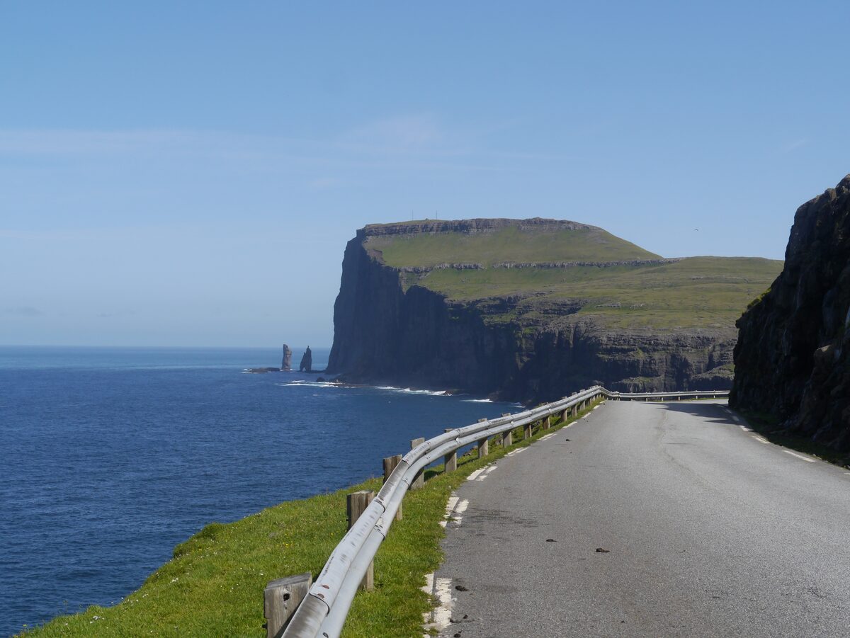 The sea stacks Risin and Kellingin below the flat-topped cliff of Eiðiskollur, seen from the coast road above the blue sea