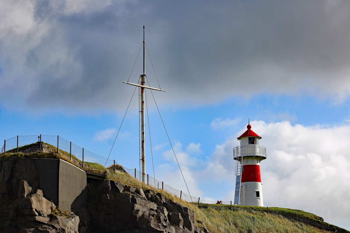 The red and white Skansin lighthouse and an old mast on the fort above Tórshavn harbor