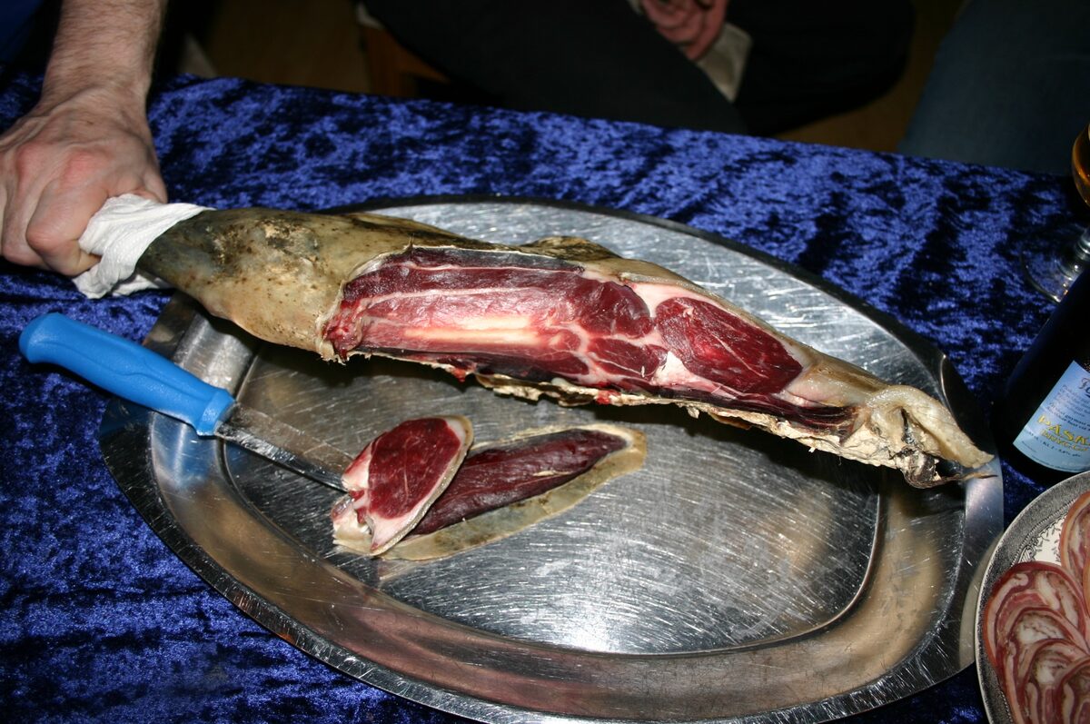 A whole dried leg of mutton (skerpikjøt) on a steel platter, with the first thin slices cut beside it