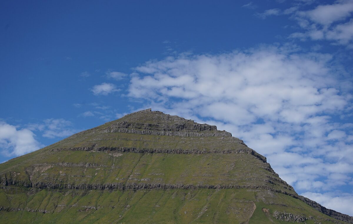 Slættaratindur, a mountain with layered cliffs and green slopes under a blue sky