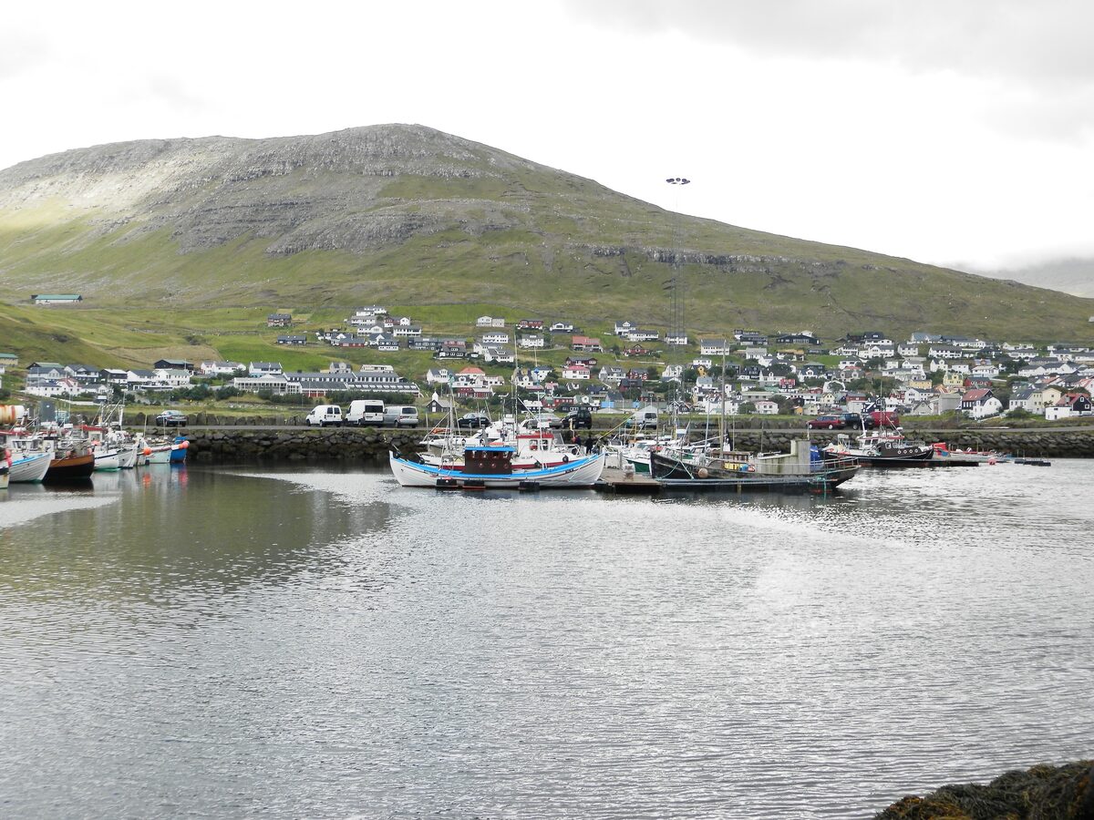 Fishing and pleasure boats in the small harbor of Sørvágur, with the town on the green slope behind