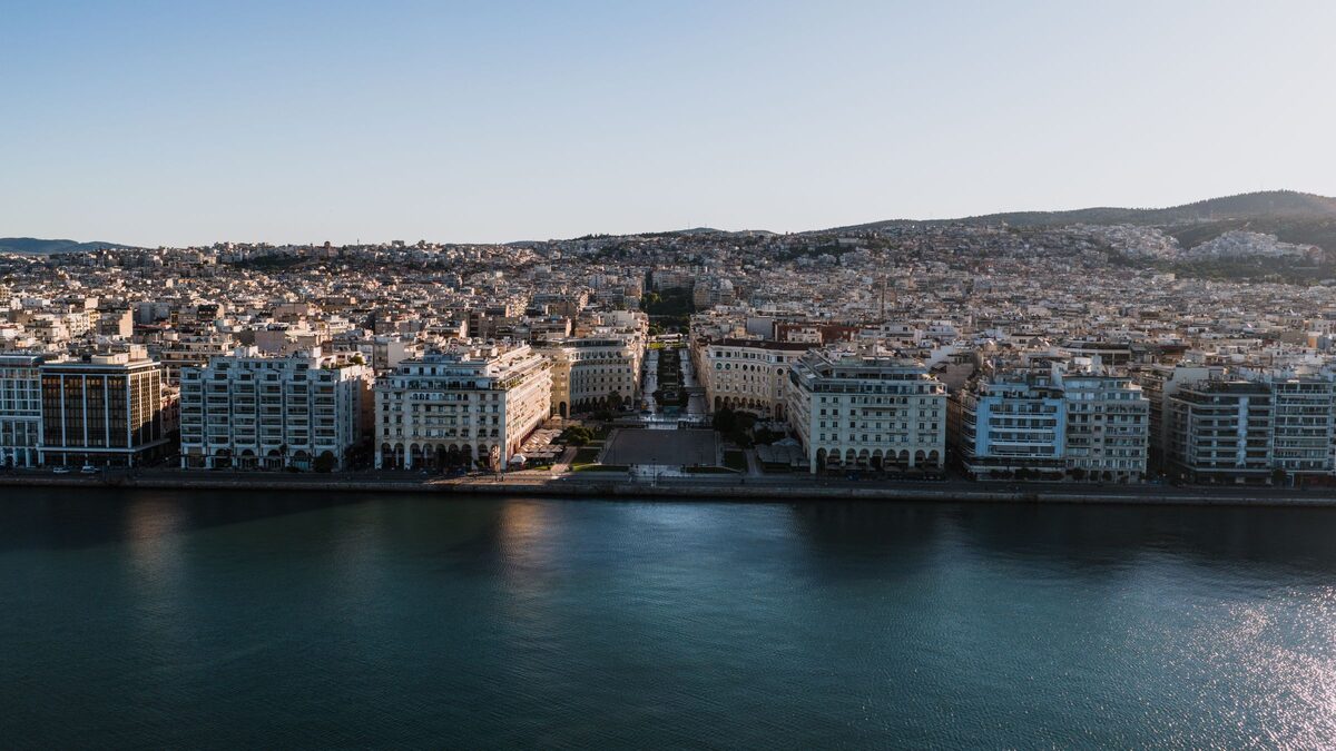Aristotelous Square seen from above the sea, with its two symmetrical rows of buildings opening onto the waterfront and the city climbing the hills behind