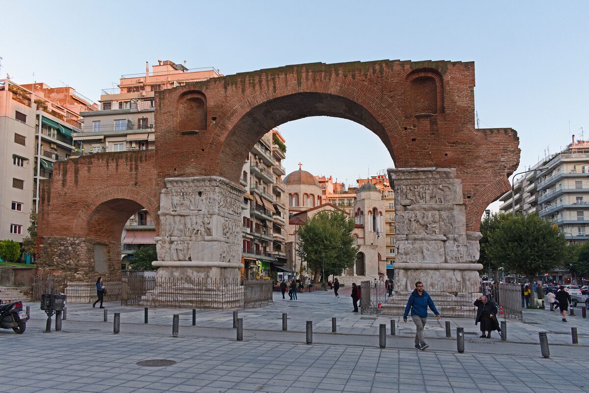The brick Arch of Galerius on Egnatia Street, with its two marble-clad pillars covered in carved reliefs and pedestrians walking through