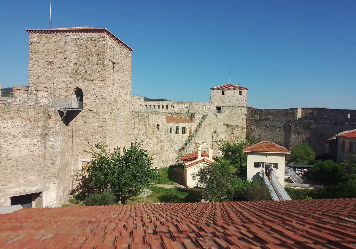 The stone towers and walls of the Heptapyrgion fortress seen over a red tiled roof, with a small chapel in the courtyard